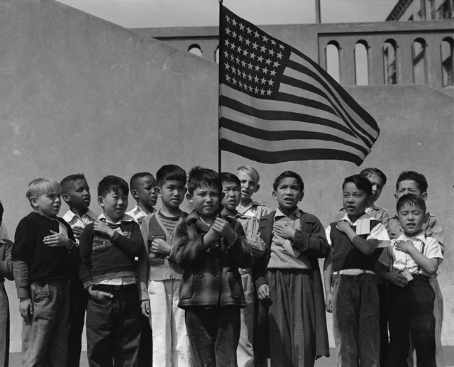Dorothea Lange. San Francisco, California. Flag of allegiance pledge at Raphael Weill Public School, Geary and Buchanan Streets. Children in families of Japanese ancestry were evacuated with their parents and will be housed for the duration in War Relocation Authority centres where facilities will be provided for them to continue their education, 1942. Courtesy National Archives.