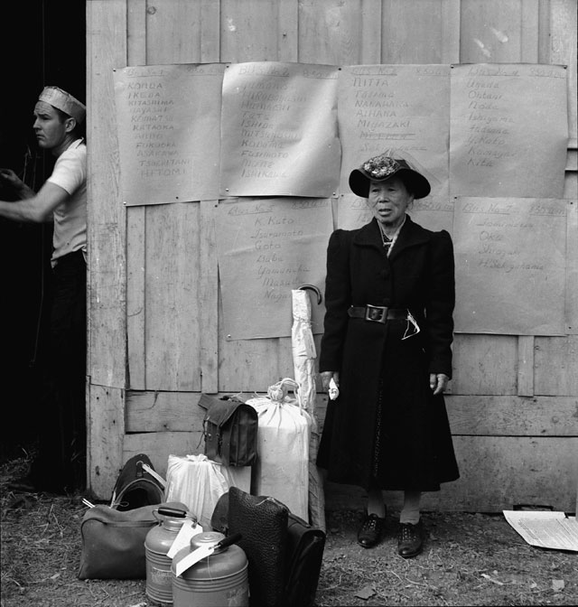 Dorothea Lange. Centerville, California. This evacuee stands by her baggage as she waits for evacuation bus. Evacuees of Japanese ancestry will be housed in War Relocation Authority centers for the duration, 1942. Courtesy National Archives.