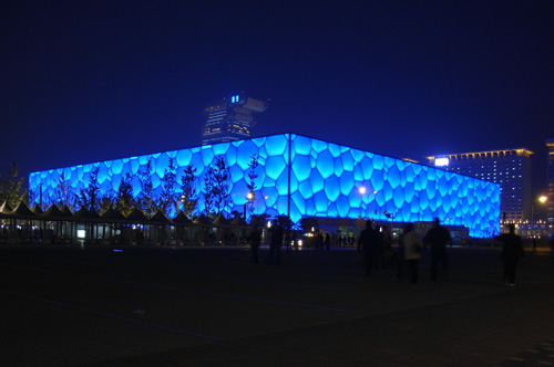 Night view of the National Aquatics Centre from the Olympic Green axis. The colour of the ETFE pillow changes to a luminous deep blue colour when illuminated from within.