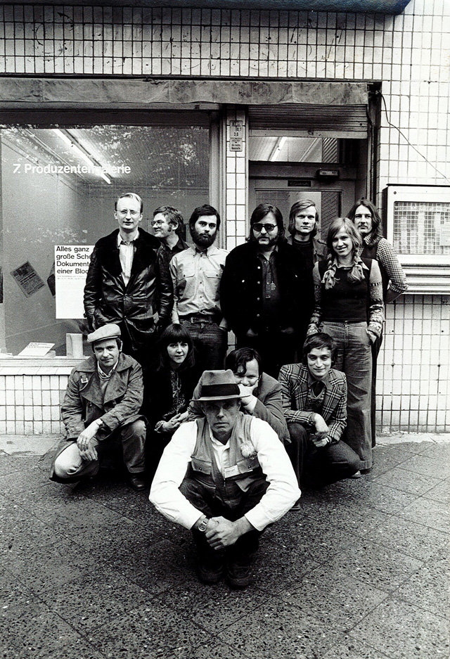 Exhibition curators and artists (back row, left to right: Klaus Staeck, Dieter Hacker, Gerhard Steidl, Christos Joachimedes, Video Cameraman, Siegrid Hacker, Martin Scutt. Front row left to right: KP Brehmer, Caroline Tisdall, Joseph Beuys, Michael Ruetz, Norman Rosenthal), taken in front of Dieter Hacker’s Produktiongalerie after the Colloquium, Berlin, 1974.