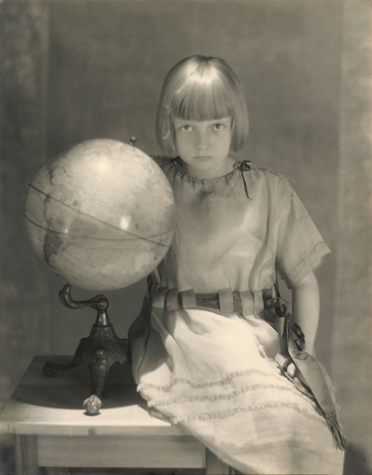 Adolph de Meyer. Young Girl Sitting [on a Small Table] Beside a Globe, Vogue, 1919. © Condé Nast.