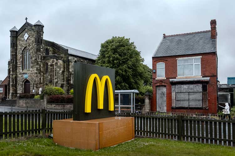 Merlin Daleman. A boarded-up house and a church behind a McDonald’s sign, Dudley, October 2017.