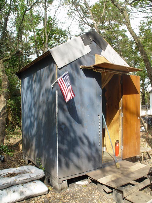 Mad Housers hut. Designer and manufacturer: Mad Housers. United States, 1987. Wood, plywood, nails, roll roofing, plastic and/or screen for windows, silver sheet insulation, paint, caulk, metal flashing, stove pipe and cinderblocks 10 ft x 6 ft x 8  ft. Photo © 2005 Salma Abdulrahman