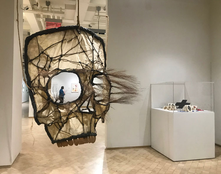 Juan Francisco Elso. El Rostro de Dios (The Face of God), 1987-88. Amate paper, branches, jute, volcanic sand, glass eyes, and iron. Courtesy of Charpenel Collection, Guadalajara, on deposit at the Museo Universitario Arte Contemporáneo, UNAM, Mexico; Background: Corazón de América (Heart of America), 1986. Silkscreen on paper, with illustration board and four-color cloth strings. Courtesy of a Private Collection, Miami, Florida. Photo: Marie Pohl.