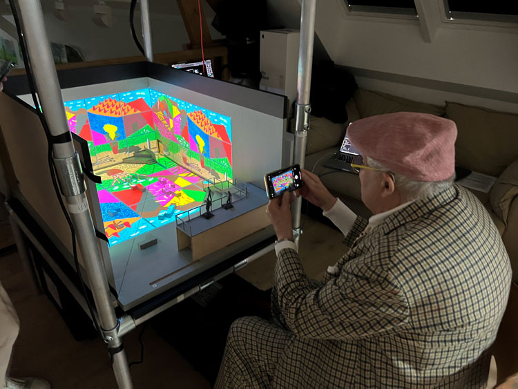 David Hockney viewing the model box containing August 2021, Landscape with Shadows. Twelve iPad paintings comprising a single work © David Hockney. Photo: Mark Grimmer.