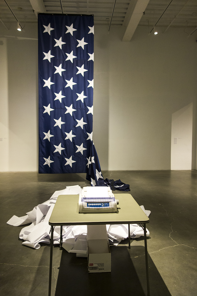 Hans Haacke, State of the Union, 2005. Nylon banner sewn by Deokallie Perfaud, 24 x 16 ft and News, 1969/2008. RSS newsfeed, paper, and printer. Dimensions and choice of news source variable. Installation view. Photo: Antonio Rivera.
