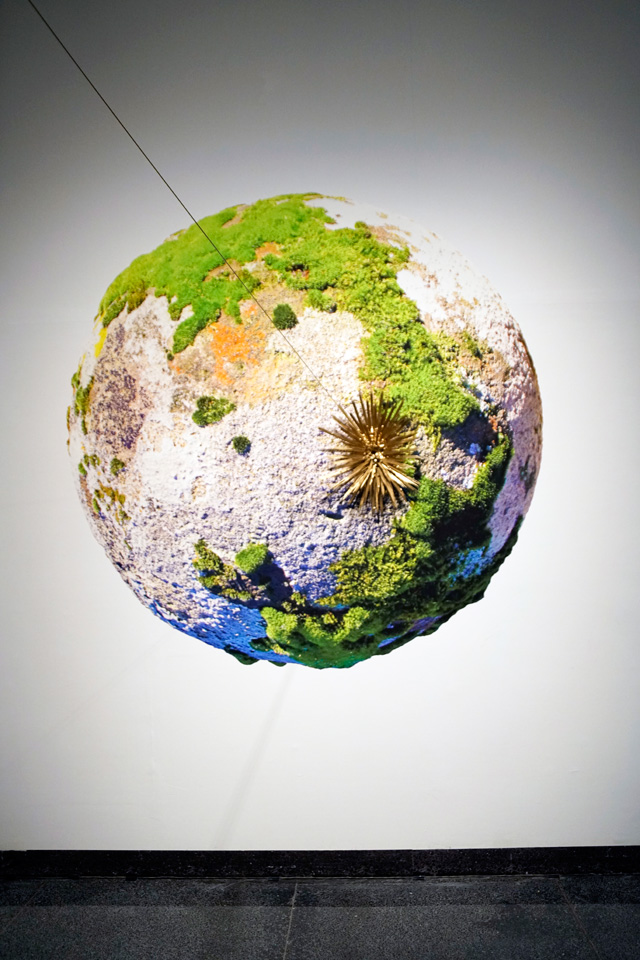 E.V. Day. Mossball - A Meditation on the Overview Effect, 2018. Mixed media installation of four components. Globe: inkjet on sintra, 84 in dia.; Sputnik: brass and resin; Raggio: gilded wood, resin and mirror; Ray: brass and monofilament, length variable. Photograph: Miguel Benavides.