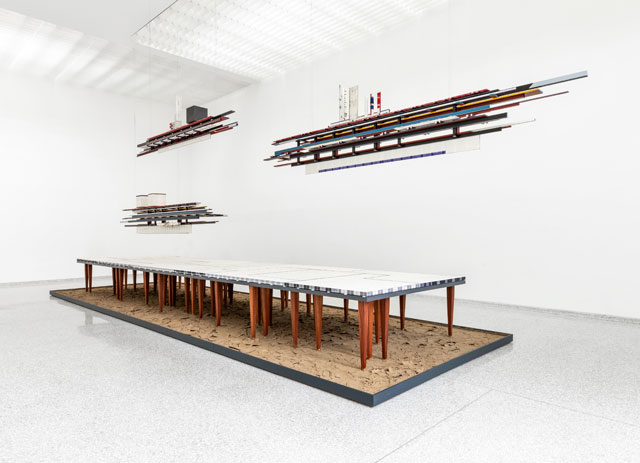 Remy Jungerman. Visiting Deities, 2018-19. Cotton textile, kaolin, dry river clay, water samples, painted wood, 58 table legs (meranti), yarn, mirror and nails, 384 x 138 x 102 in (975 x 350 x 260 cm). Photo: Aatjan Renders.