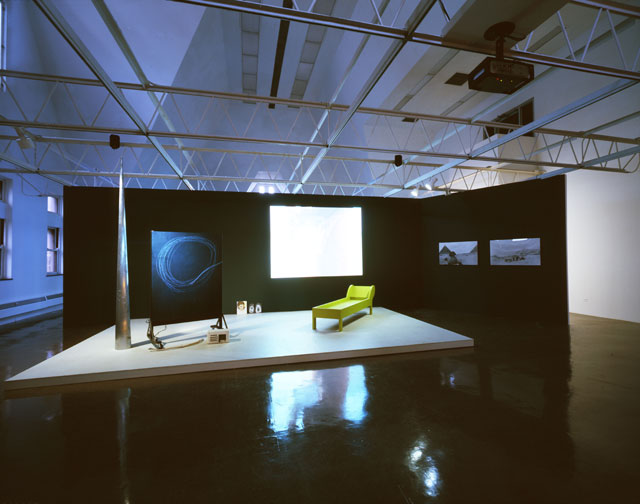 Joan Jonas. Lines in the Sand, 2002. Installation Video (Lines in the Sand 2002/2005. Colour, sound, 47:45 min), projection, blackboard, wooden structure, paint, video (Pillow Talk, 2002, colour, sound), monitor with performance video, green wooden couch, sand and relief box, plaster, photographs, paintings), dimensions variable. Museu d'Art Contemporani de Barcelona, 2007. Photograph: Juan Andres Pegoraro. © 2018 Joan Jonas : Artists Rights Society (ARS), New York : DACS, London.