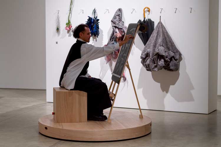 Laura Lima, The Drawing Drawing, 2026. Mechanised platforms (wood, metal, motors, electrical components, wheels), life model, paper, pencils and pens, still life display, ICA visitors. Installation view, Institute of Contemporary Arts, London. Photo: Anne Tetzlaff.