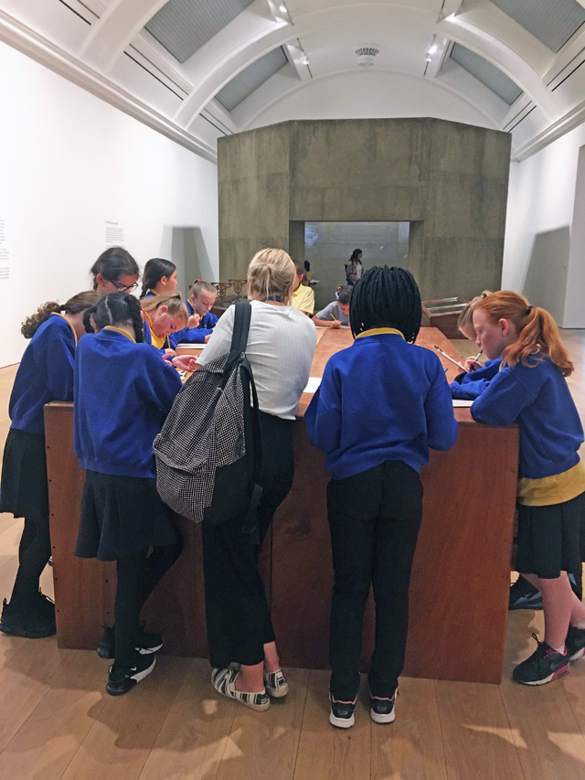 Ibrahim Mahama, The Archive, school group and teacher cluster around workbenches, with Silo in the distance. Installation view, Whitworth Art Gallery, Manchester, 2019. Photo: Veronica Simpson.