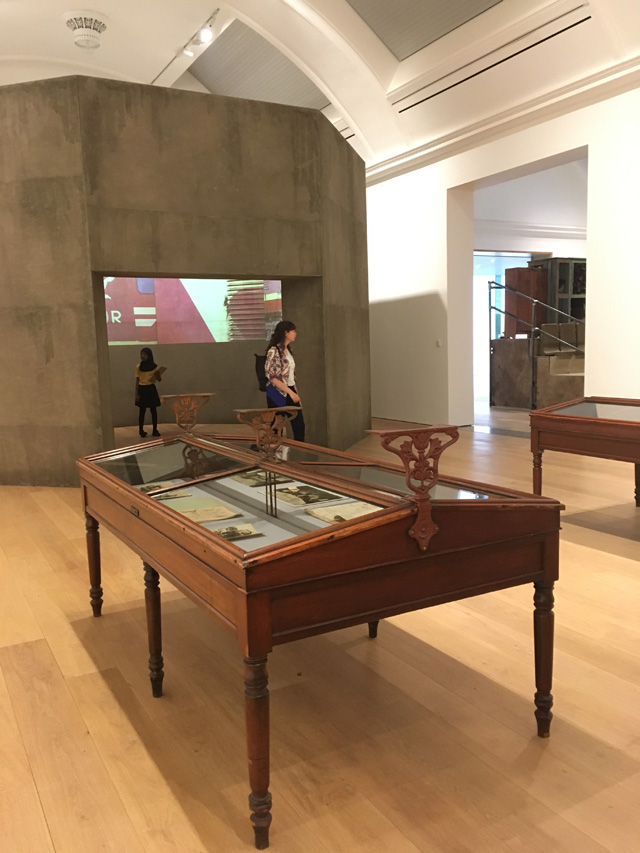 Ibrahim Mahama, Silo and projections in background, glass cabinets with archive material in foreground. Installation view, Whitworth Art Gallery, Manchester, 2019. Photo: Veronica Simpson.