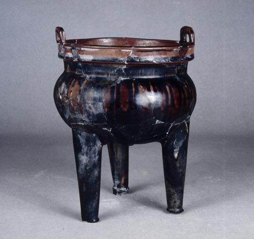 Incense burner with black glaze. Ming dynasty Yongle (1403-24). Height: 21.2 cm. Diameter at mouth: 14.5 cm. This Incense burner has two ears and three legs. The body is incised with designs of grass and chrysanthemum but unclear. It is covered with red glazed but uneven.