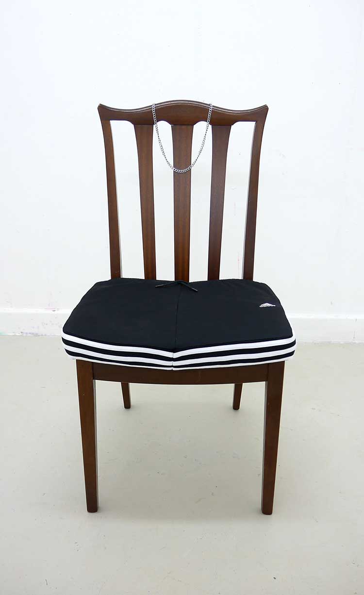 AC Larsen, Supper Time, 2024. Vintage early 1990s G Plan dining chair, Adidas Originals tracksuit, stainless steel Cuban chain. Courtesy of the Artist.