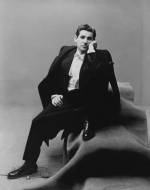 Leonard Bernstein, conductor and composer, wearing a tuxedo, sitting on a group of carpeted boxes. Portraits of people of the 