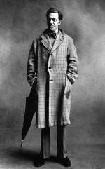 Cecil Day Lewis, poet, wearing a three-button, checked overcoat, hands in the pockets, with an umbrella.