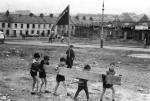 Eamon Melaugh. These children are either engaged in strengthening street barricades or bringing some firewood home for the house. The boy with the flag is striking a particularly good revolutionary pose for one so young! Note the 'Derry Merry, Derry Free' banner in the background. The photograph may have been taken around the time of the Liberation Fleadh, 30 August 1969. Lecky Road, Bogside, Derry.