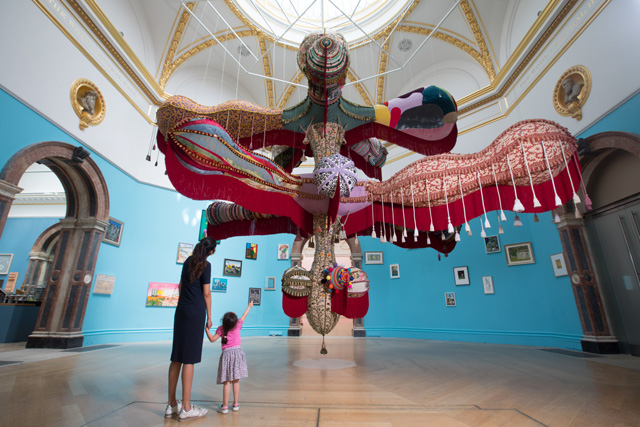 Joana Vasconcelos. Royal Valkyrie. Handmade woollen crochet, felt appliqués, ornaments, fabrics, inflatable, power supply unit and steel cables, 625 x 600 x 900 cm. © Royal Academy of Arts. Photography: David Parry.