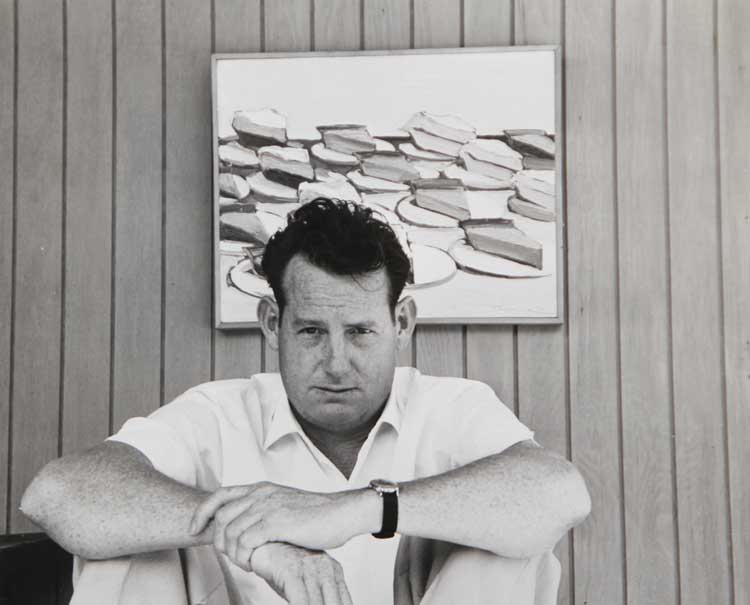 Wayne Thiebaud in his studio in Sacramento with his painting Pies in the background, 1961. Photo: Betty Jean Thiebaud. Collection of the Wayne Thiebaud Foundation. © Wayne Thiebaud/VAGA at ARS, NY and DACS, London 2025.
